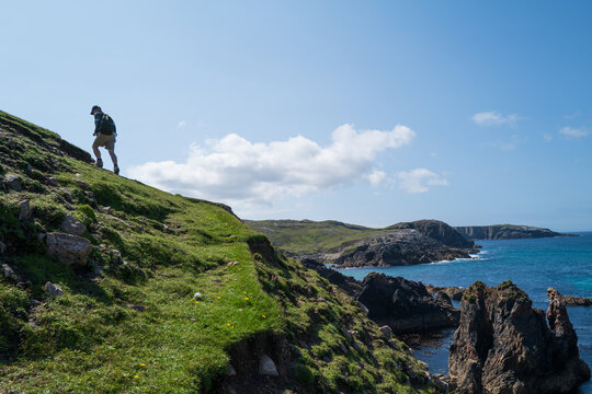 Male hiker walking up a headland on the coast of The Isle of Lewis.