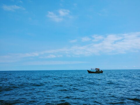 Small fishing boat floating on calm deep blue sea under clear bright sky with soft natural daylight