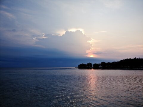 Dramatic sunset over a calm ocean horizon with soft purple clouds and golden light reflecting on water
