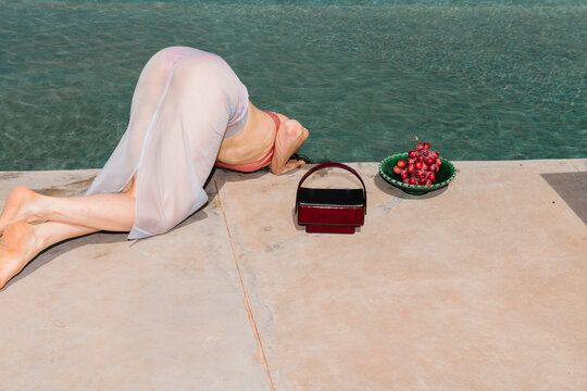 Poolside Model Reaching Over Water With Purse