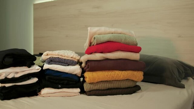 Placing a stack of warm folded clothes at the edge of a wardrobe shelf while organizing seasonal autumn and winter garments for the colder months.