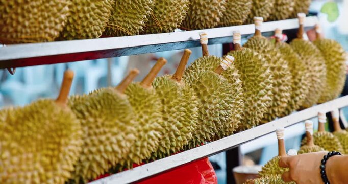 Durian fruit selected by customer from shelf at outdoor market stall, tropical fruit commerce in Southeast Asia, commercial food retail.