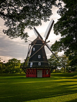 Copenhagen, Denmark - 30.07.2017: Historic dark wooden smock windmill with red base on green lawn under dramatic overcast sky