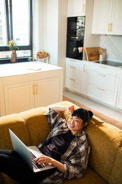 Relaxed young adult using laptop on sofa in modern home kitchen