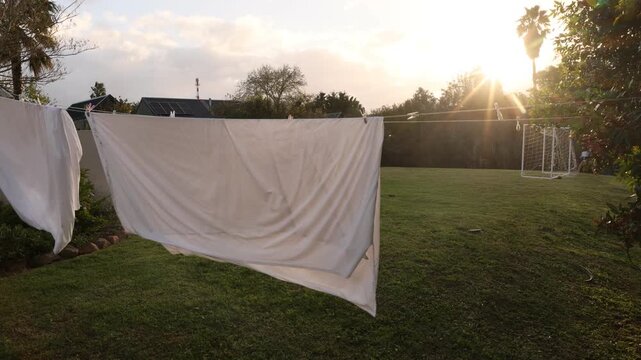 teenage boy practicing kicking soccer ball through white sheets drying on a clothes line at sunset