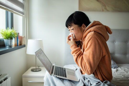 Sick woman working on laptop in bed at home
