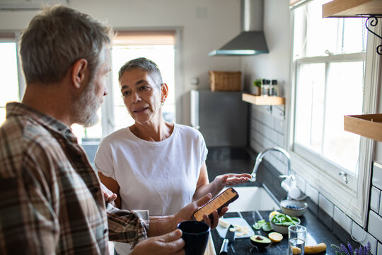 Senior couple discussing recipe on smartphone in home kitchen
