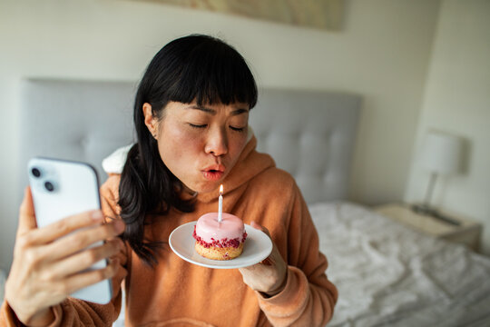 Woman blowing out birthday candle during video call at home