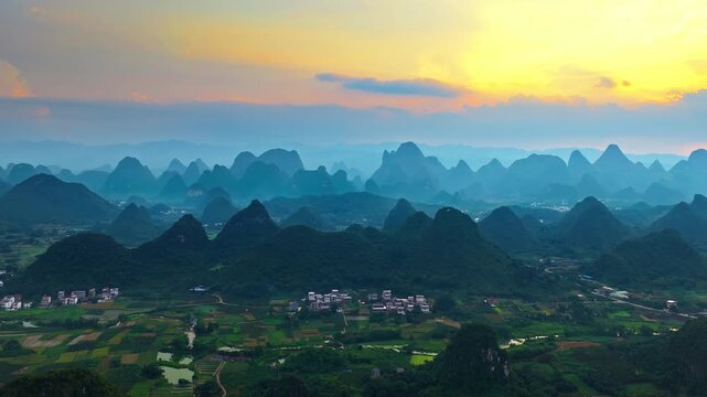 Sunrise aerial panorama of misty karst mountains, rural villages and patchwork farmland in Guilin, China, ideal for travel and nature tourism.