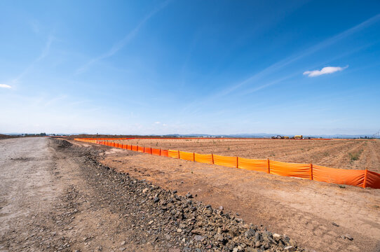 Eugene, Oregon, United States - 16 August 2026: View of the construction site for the new Amazon warehouse center near Eugene Airport, featuring a cleared field with orange silt fencing.