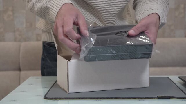Hands open the shipping box and take out a new black external hard drive, Man unboxing electronic device from a cardboard bo