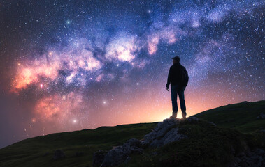 Fototapeta premium Glowing Milky Way and man on mountain peak at starry night. Silhouette of a guy on the hill, sky with bright stars. Galaxy. Space landscape with milky way. Nightscape. Travel background. Concept