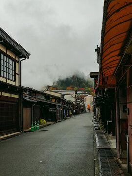 Takayama, Gifu, Japan - 01 September 2026: View of historic streets in Takayama with traditional wooden merchant houses, misty mountains, and autumn foliage under a cloudy sky.
