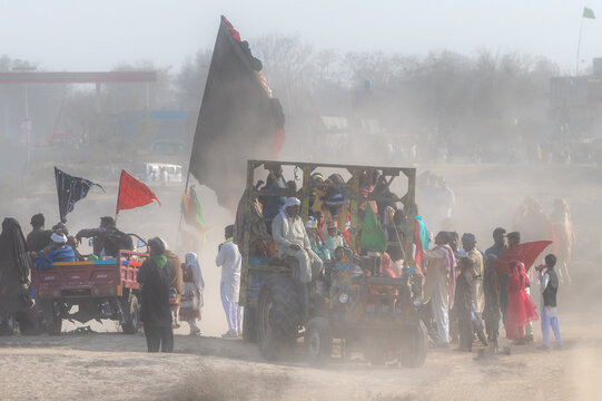 Okara, Punjab, Pakistan - 13 March 2024: View of devotees traveling on a tractor during the annual Urs festival at the shrine of Hazrat Daud Bandagi Kirmani in a dusty landscape.