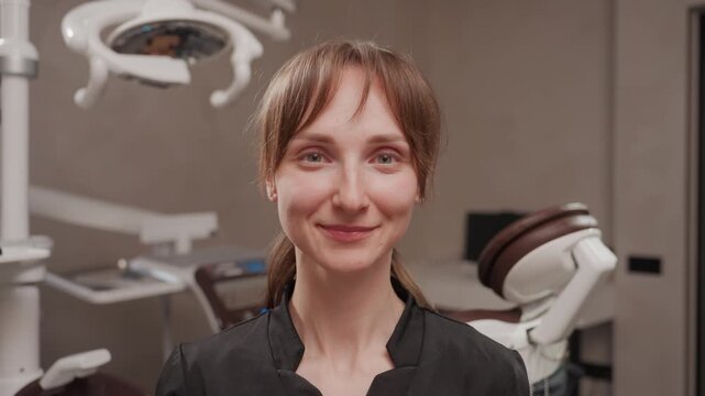 Close up of dental hygienist wearing protective face shield in clinic adjusting and removing transparent visor while standing near patient chair and overhead light. Dental office setting