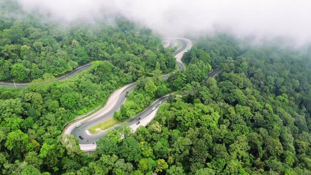 Aerial view of the winding road at Panatapan Berastagi surrounded by dense tropical forest and misty hills in Berastagi, North Sumatra, Indonesia.