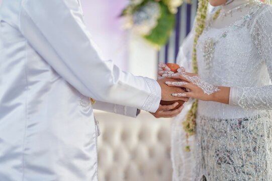 Indonesian wedding ceremony showing bride and groom hands with soft natural light and traditional white lace attire
