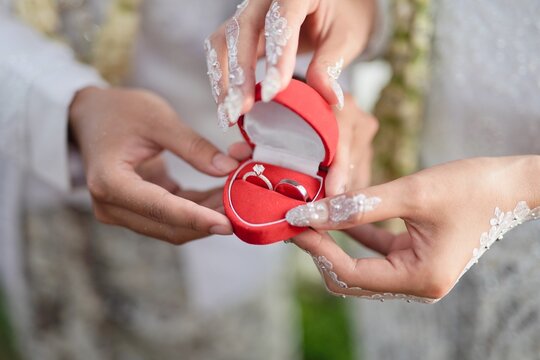 Close up of an Indonesian bride and groom holding a red velvet wedding ring box with soft lighting