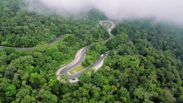 Aerial view of Panatapan Berastagi winding road surrounded by lush tropical forest and misty hills in Berastagi, North Sumatra, Indonesia.
