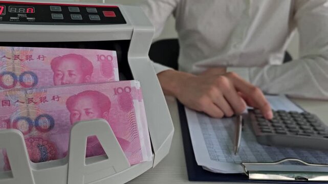 Counting cash in a bank using a money counter and calculator in China