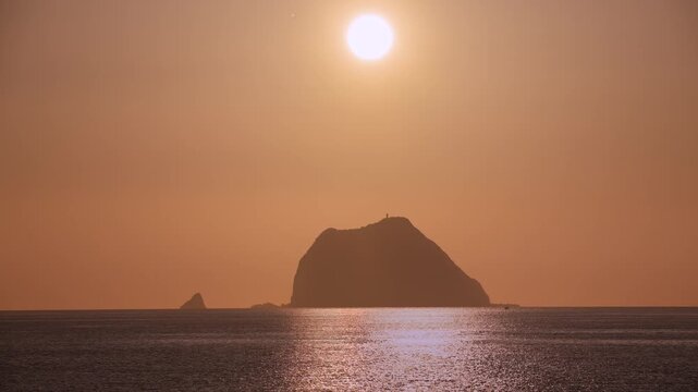 A beautiful golden sunrise over the silhouette of Keelung Islet in Taiwan, with the sun shining brightly in an orange sky over the calm ocean.
