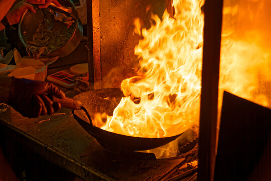 The vendor of a food stall frying noodles and stirring the pan on the furious fire, in Ruifeng Night Market, where many street snacks can be savored, in Zuoying District, Kaohsiung City, Taiwan