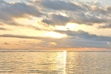 Obraz premium Vertical view of the sun bursting through low clouds over the calm ocean, casting a golden reflection on the water and the sandy shore of Sanur beach in Bali, Indonesia.