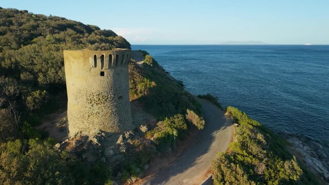 Marine de Meria Genoese tower Corsica drone orbit over tower pull back reveal seaside houses and winding D80 coastal road in golden sunset light. Cap Corse Cinematic 4K drone video