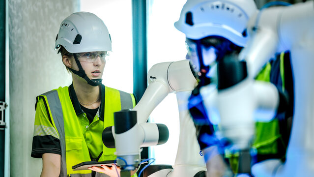 Female robotics engineers work side by side calibrating a small white robot arm on the bench during industrial automation work, showcasing smart manufacturing and robotics technology