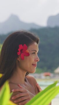 Beach beauty woman natural girl looking serene on tropical beach. Asian bikini model wearing hibicus flower body care wellness and spa pampering. Raw vertical video of real woman model without makeup