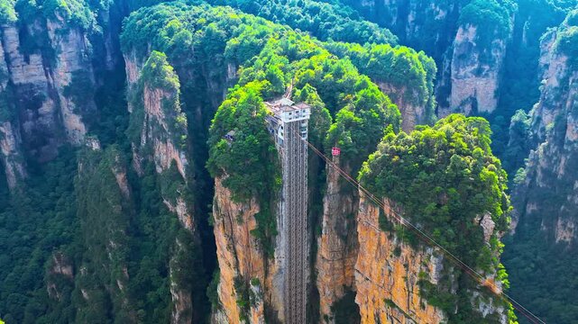 Dramatic aerial view of an outdoor cliff elevator rising beside forested sandstone pinnacles in Zhangjiajie, China, showcasing tourism infrastructure and natural scenery.