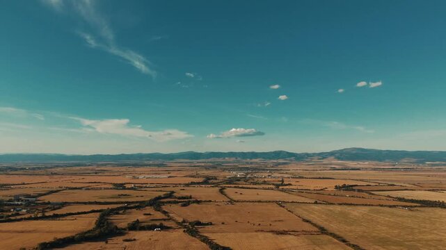 Timelapse of vast golden agricultural fields and distant mountains under a blue sky