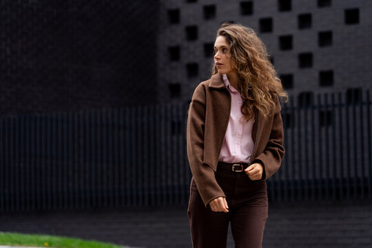 Young woman in brown jacket looking away against textured wall