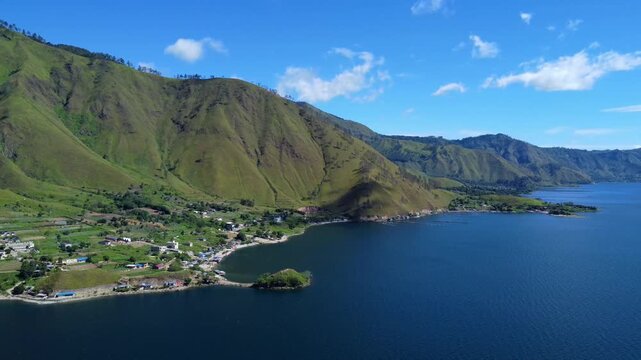 Aerial view of Lake Toba with lush green hills and a small village along the shoreline in Parapat, North Sumatra, Indonesia.
