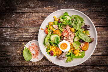 Tuna salad with tomatoes, cucumber, corn, olives , eggs and onion on wooden background, top view....