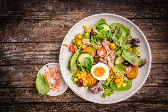Tuna salad with tomatoes, cucumber, corn, olives , eggs and onion on wooden background, top view. High quality photo