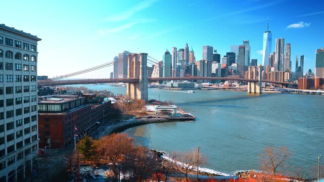Elevated view of Brooklyn Bridge above East River. Empire Stores lines the shore as skyscrapers and a carousel pavilion rise beyond the water.