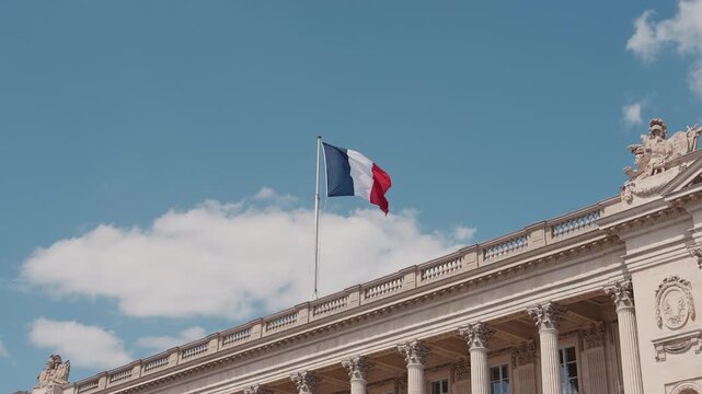 French national tricolor flag waving in slow motion on the roof of H&ocirc;tel de la Marine in Place de la Concorde, Paris. Blue sky with white clouds in the background. High quality 4K video.