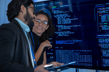 Fototapeta premium Two tech professionals examine a neural network visualization projected on a large display in a dark AI operations center.