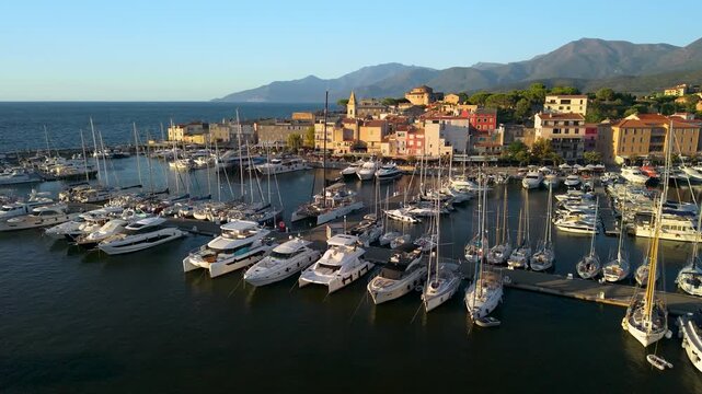 Saint Florent Corsica 4K drone video part 2. Ascending fly out from town marina to reveal entire coastal town in golden hour sunset light. High end luxury travel b roll stock footage