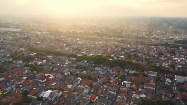 Aerial view of dense residential rooftops and a mosque illuminated by warm sunset light in Depok, West Java, Indonesia.