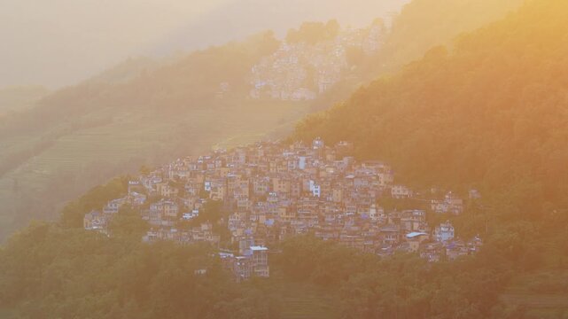 Aerial view of a traditional village nestled in the mountains during golden hour in Honghe Hani and Yi Autonomous Prefecture, Yunnan, China.