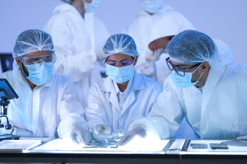 A cleanroom technician and colleague study a reflective silicon wafer closely in a high-technology...
