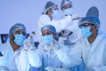 A semiconductor cleanroom team study a sample under bright inspection light wearing full coveralls...