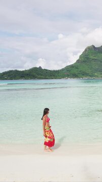 French Polynesia Vacation Travel woman walking on paradise motu beach on Bora Bora with Mount Otemanu wearing traditional pareo and Bikini in Tahiti. Raw vertical video of real woman without makeup