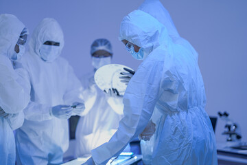 Masked cleanroom workers study a sample under bright inspection light in a white semiconductor...