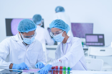 A diverse research team compare liquid samples in a test-tube rack in a bright modern laboratory...