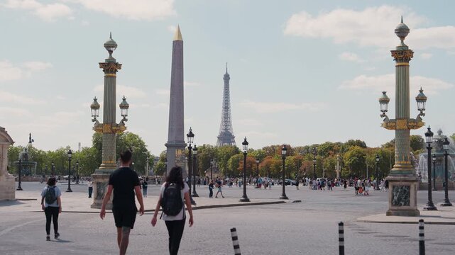 Static shot of Place de la Concorde with the Luxor Obelisk, ornate lamp posts, and Eiffel Tower in the background as tourists walk by in Paris, France. High quality 4K B-roll video.