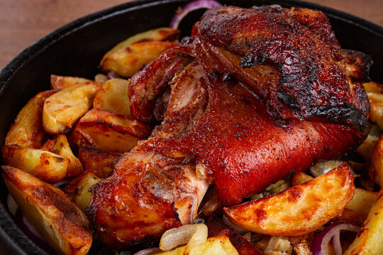 Roasted pork knuckle, with potato slices, on a round pan, on a wooden table, homemade, no people,