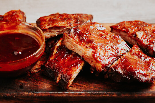 BBQ ribs with sauce served on a wooden board in a kitchen setting